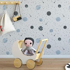 a small doll sitting in a wooden toy car next to a wall with planets on it