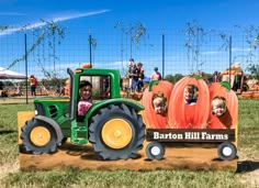 two children are riding on a tractor with pumpkins in the back and behind them