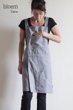 a woman wearing an apron looking at her cell phone while standing in front of a white wall