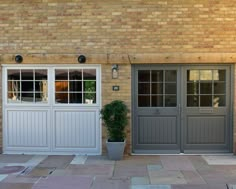 two double doors are open in front of a brick building with a potted plant