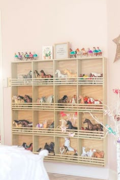 a wooden shelf filled with lots of toy horses next to a white bed in a room