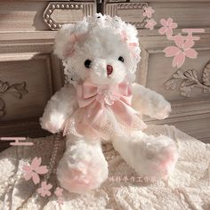 a white teddy bear with pink bows on it's head sitting on a bed