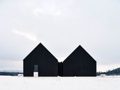 two black buildings in the middle of a snow covered field