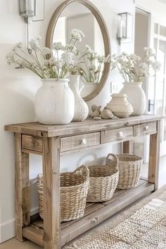 a wooden table with baskets and flowers on it in front of a round mirror above