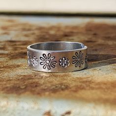 If you love flowers and/or being outdoors, this ring is perfect for you! Daisy flowers in two sizes adorn this hand crafted adjustable (midi) ring. I personally hand stamp all of the lettering and designs in my studio. Each design is hand aligned and punched into the metal, so the placement of the wording and designs will vary slightly from piece to piece. After stamping, I darken the impressions so they stand out. To retain the contrast, it is highly recommended that the piece is not exposed to Handmade Adjustable Flower Ring For Anniversary, Adjustable Hand Stamped Midi Rings, Adjustable Hypoallergenic Flower Promise Ring, Adjustable Stamped Flower Jewelry, Personalized Silver Adjustable Flower Ring, Adjustable Flower Ring For Everyday Wear, Adjustable Hand Stamped Midi Rings As Gifts, Handmade Adjustable Engraved Ring For Everyday, Flower Shaped Engraved Adjustable Promise Ring