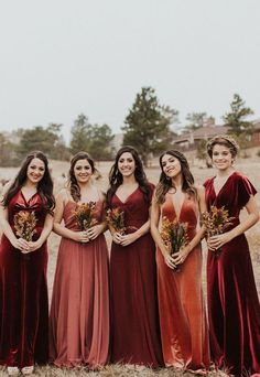 a group of women standing next to each other in long red dresses holding bouquets