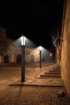 two street lights on the side of a brick building at night with no one in it