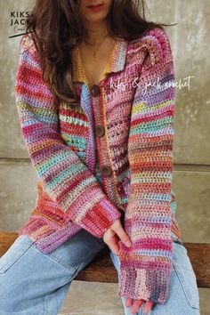 a woman sitting on top of a wooden bench wearing a colorful knitted cardigan