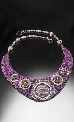 a purple beaded necklace with two circular beads hanging from it's center, on a black background