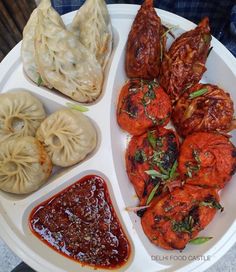 a white plate topped with meat and dumplings next to sauces on a table