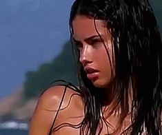 a close up of a woman with wet hair and no shirt on standing near the water