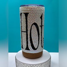 a glass with the word ho on it sitting on top of a white stand next to a blue wall