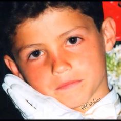 a young boy wearing white gloves and a red bow tie with flowers in the background