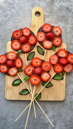 strawberries are arranged on sticks and placed on a cutting board