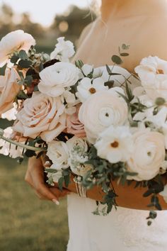 a bride holding a bouquet of white and pink flowers on her wedding day at sunset