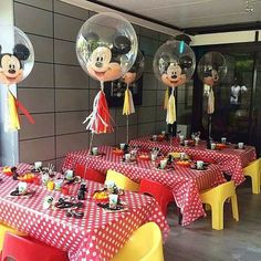 mickey mouse balloons are hanging from the ceiling at a table with red and yellow clothed tables