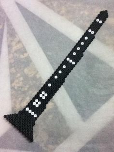 a black and white beaded bracelet with cross stitching on the end, sitting on top of a piece of fabric