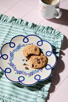 two chocolate chip cookies on a blue and white plate next to a cup of coffee