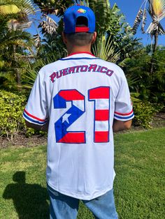 Tainowears Puerto Rico Baseball Jersey. This premium white jersey features bold "PR" embroidery, the iconic Coqui and El Morro in translucent artwork, and vibrant Puerto Rican flag colors on the sleeve. With "WEPA!" embroidered to honor the island’s energy, "Puerto Rico" on the back in PR colors, and the legendary #21 with an intricate flag design, this jersey embodies Puerto Rican pride. Premium PR Embroidery: Highlights "Puerto Rico" pride in vibrant detail. Iconic Coqui & El Morro Design: Add Puerto Rico Culture Clothes, White College Jersey With Letter Print, College White Jersey With Letter Print, Throwback Jersey With Letter Print For Game Day, Baseball Season Fan Gear Jersey With Letter Print, White Team Spirit Jersey For College, White Jersey For College With Team Spirit Style, White College Baseball Jersey With Team Logo, White Baseball Jersey With Team Name