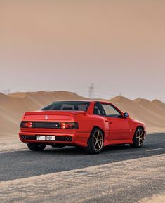 the red car is driving down the road in front of some sand dunes and hills