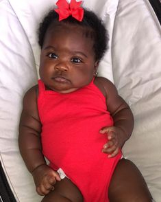 a baby in a red bodysuit with a bow on her head is laying down