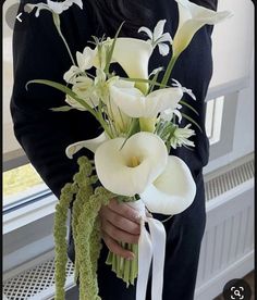 a woman holding a bouquet of white flowers in her hands and wearing a black sweater