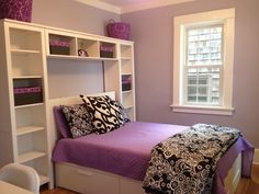 a bedroom with purple walls and white bookcases on the bed, along with black and white pillows