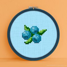 a cross - stitch blue flower is shown in a round frame on an orange wall