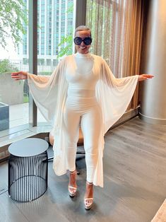 This elegant ensemble combines a sleek, form-fitting white jumpsuit with a flowing, sheer cape, creating a striking blend of modern sophistication and timeless grace. The outfit's minimalist design is accentuated by its clean lines and pure white fabric, making it perfect for high-profile events or stylish gatherings. The sheer cape adds a touch of ethereal charm, while the overall silhouette flatters the figure, offering both comfort and style. Paired with bold accessories, this outfit exudes c Sheer Cape, Cape Jumpsuit, Outfits Minimalist, Plus Jumpsuit, Bold Accessories, Fabric Making, White Jumpsuit, Plus Dresses, New Wardrobe