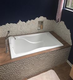 a bathroom with a large white bathtub next to a window and rug on the floor