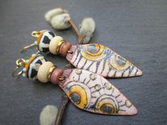 These earrings feature tribal enameled copper charms by Verreetcuivre in France. The leaf shaped charms are decorated with a sun motif set against a cream and black zebra striped background. Above the charms are mauve coconut wood beads followed by gold disc beads. Next are cream coconut wood beads. These support tribal lamp-work glass beads, also by Verreetcuivre. The lamp-work beads are black with white stripes on the bottom and orange with aqua raised glass dots on top. Bi-cone brass beads to Bohemian Teardrop Jewelry With Artistic Design, Bohemian Hand Painted Metal Jewelry, Bohemian Hand Painted Copper Jewelry, Bohemian Hand Painted Enamel Jewelry, Hand Painted Bohemian Enamel Jewelry, Bohemian Enamel Earrings Nickel Free, Handmade Bohemian Enamel Jewelry, Bohemian Hand Painted Copper Earrings, Hand Painted Copper Bohemian Earrings