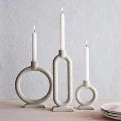 three candles are placed in the shape of circles and rings on a table next to plates