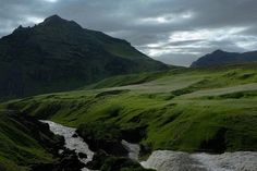 a river running through a lush green valley next to a mountain covered in grass and rocks