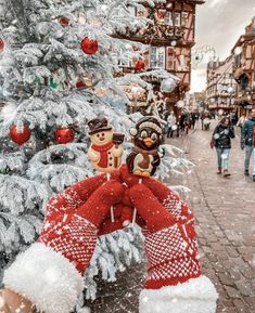 a christmas tree in the middle of a street with people walking by and trees covered in snow