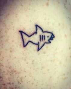 a small shark tattoo on the back of a woman's left shoulder, it is black and white