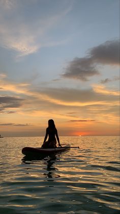 a woman sitting on top of a surfboard in the middle of water at sunset