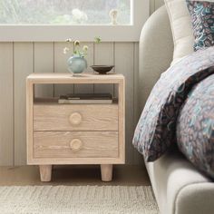 a nightstand with two drawers in front of a window and a bed next to it