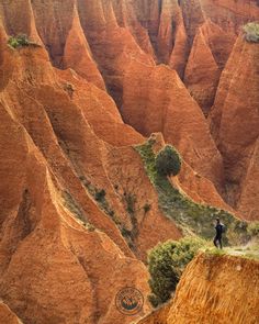 a man standing on top of a mountain next to tall red hills covered in trees