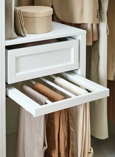 an open drawer in a closet with clothes hanging on the wall and folded linens