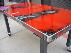 a red table sitting on top of a sidewalk next to a parking meter and building