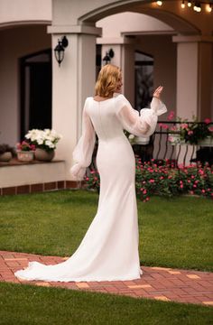 a woman in a white wedding dress standing on a brick walkway with her arms outstretched