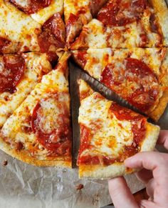 a person cutting into a pizza on top of a wooden board with cheese and pepperoni