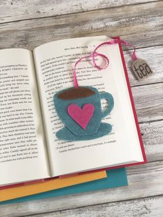 an open book with a felt coffee cup on it and a pink heart hanging from the pages