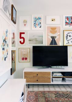 a flat screen tv sitting on top of a white dresser next to a wall filled with pictures