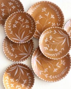 six brown and white plates sitting on top of each other, with leaves painted on them