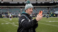 a man holding an orange cell phone in front of his face on a football field