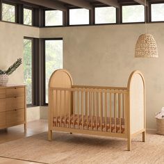 a baby's crib in the corner of a room with wooden furniture and large windows