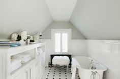 a white bath tub sitting under a window next to a sink in a room with black and white tile flooring