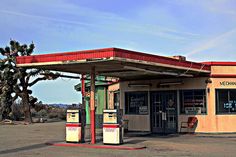 an old gas station sits empty in the middle of a deserted desert area with palm trees