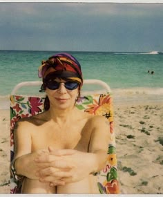 a man sitting in a lawn chair on the beach wearing sunglasses and a bandana